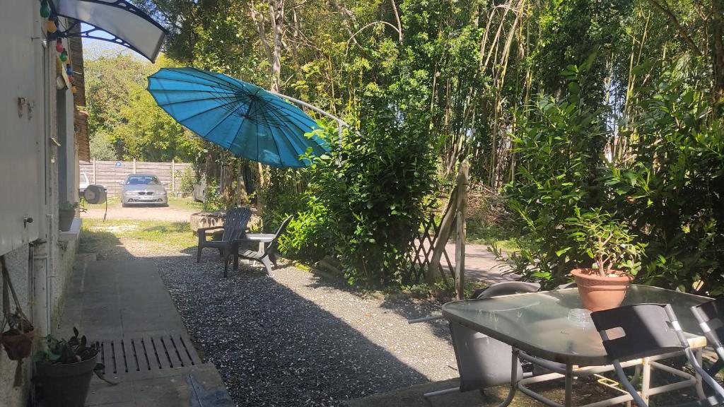 a blue umbrella is flying over a table and a table with chairs at Logement entier proche des châteaux - 1 à 6 Pers - in Barsac