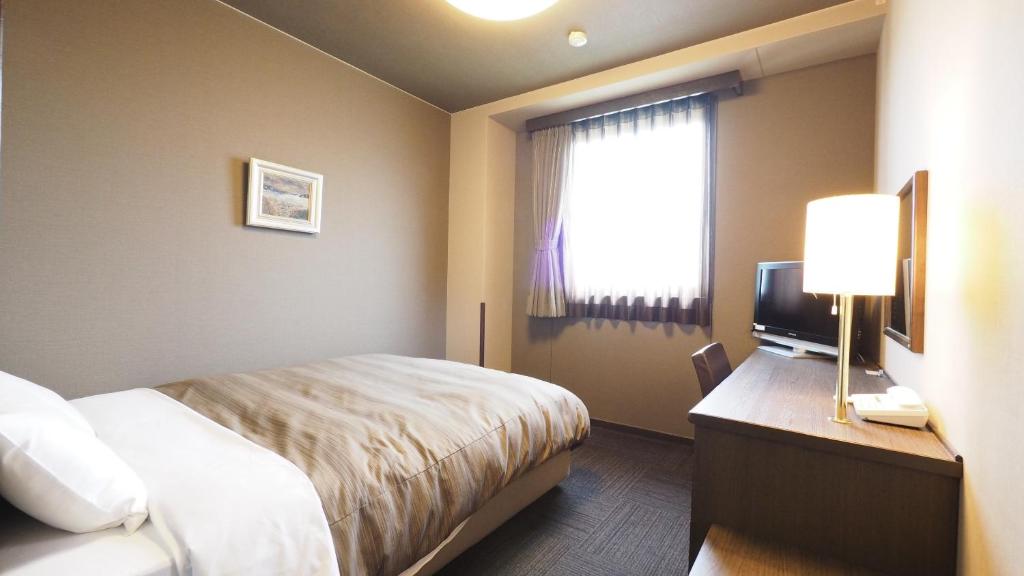 a hotel room with a bed and a window at Hotel Route-Inn Court Matsumoto Inter in Matsumoto