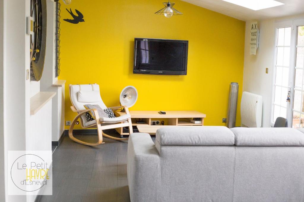 - un salon avec un canapé et une télévision sur un mur jaune dans l'établissement Le Petit Havre d'Esneval - proche d'Etretat -, à Criquetot-lʼEsneval