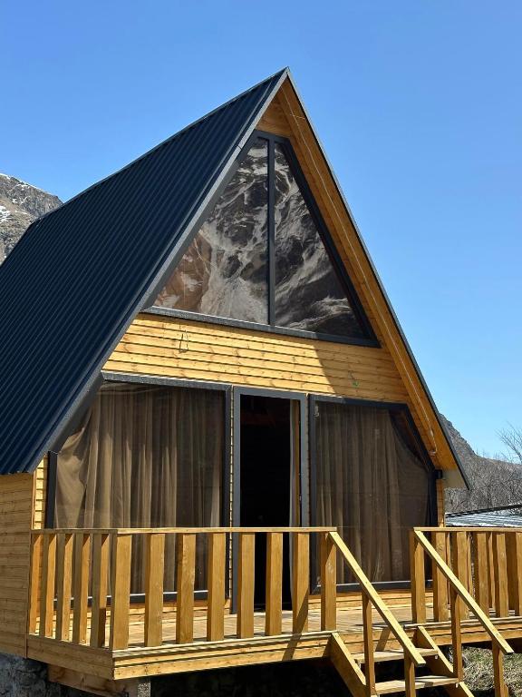a cabin with a gambrel roof and a deck at Sunny Side Cottage in Kazbegi