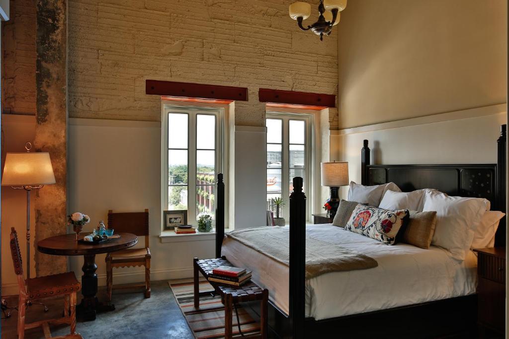 a bedroom with a bed and a table and windows at Hotel Emma at Pearl on the Riverwalk in San Antonio