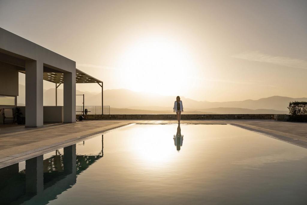 a woman standing on the edge of a swimming pool with the sun setting at Diktamon Retreat Luxury Villa in Foinikiá