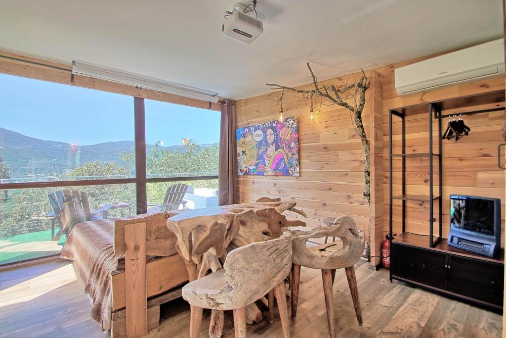 une salle à manger avec une table, des chaises et une grande fenêtre dans l'établissement Sublime cabane perchée clim et cinéma vue panoramique - Le Mas des farachess, à Solliès-Toucas