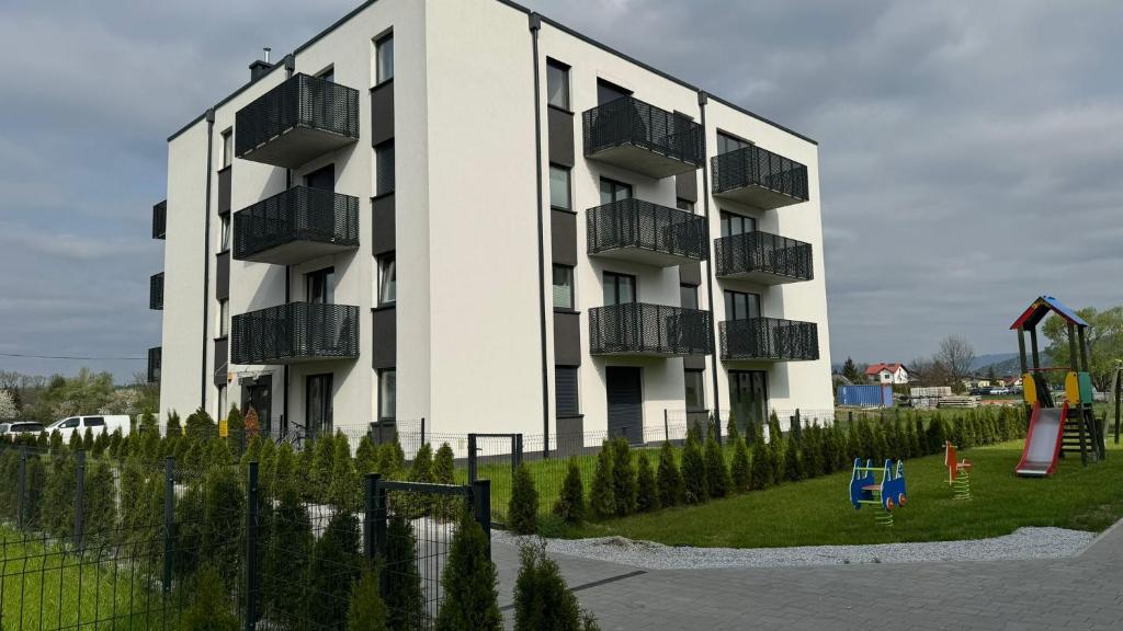 a large white building with balconies and a playground at Apartament Pastelove Żywiec in Żywiec