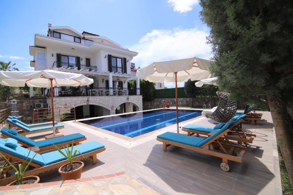 a pool with chairs and umbrellas next to a house at Villa TN - Fethiye in Fethiye