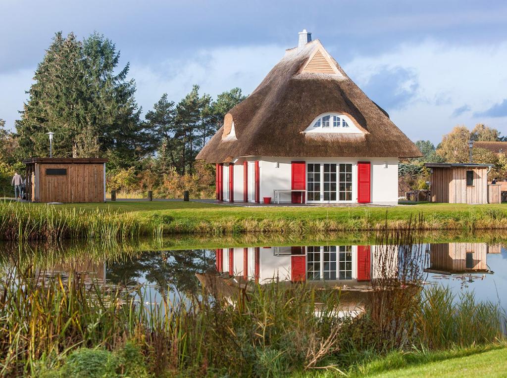 Casa con techo de paja y reflejo en un estanque en Ferienhaus Haubenlerche 63 - Haus Marilyn en Fuhlendorf