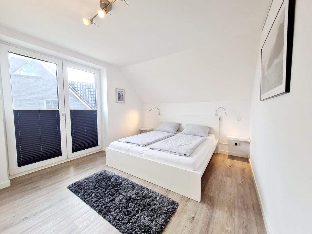 ein weißes Schlafzimmer mit einem Bett und zwei Fenstern in der Unterkunft Sandbank in Sankt Peter-Ording