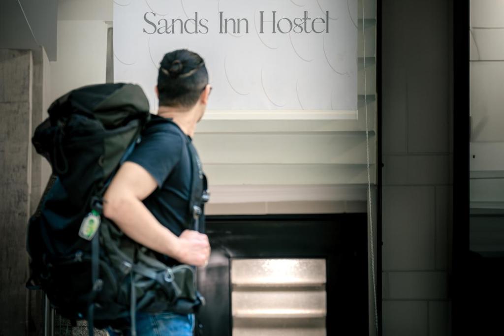 利雅德的住宿－Sands Inn Hostel，背着背包站在标志前的人