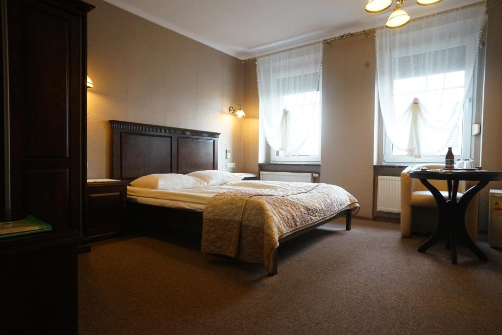 a bedroom with a bed and a table and windows at Hotel Alexandra in Olesno