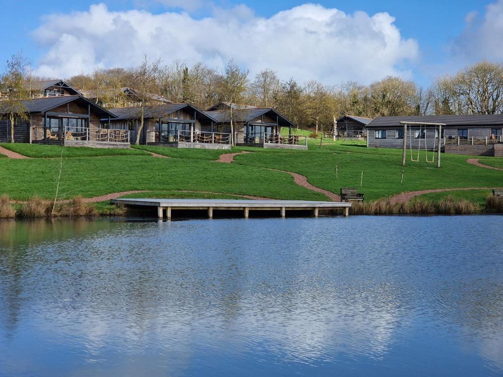 a house with a dock next to a lake at Zen Jungle Retreat - Log Cabin Stays, Transformational Retreats & Holistic Wellness near Bude - A 40 Acre Retreat with 5 Lakes, Woodland, Firepits, Bistro & Bars in Holsworthy