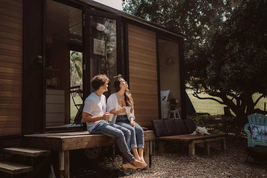 zwei Personen, die auf einer Bank vor einem Haus sitzen in der Unterkunft Cockatoo Cabin in Palmwoods