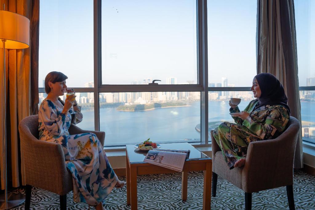 Dos mujeres sentadas en sillas en una habitación con bebidas en Copthorne Hotel Sharjah, en Sharjah