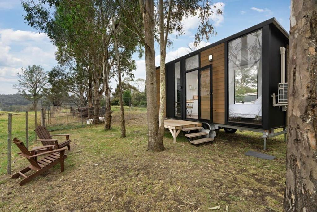 a black tiny house in a forest with benches at The Stockmans Camp 1 - Sunset Tiny House in Buchan