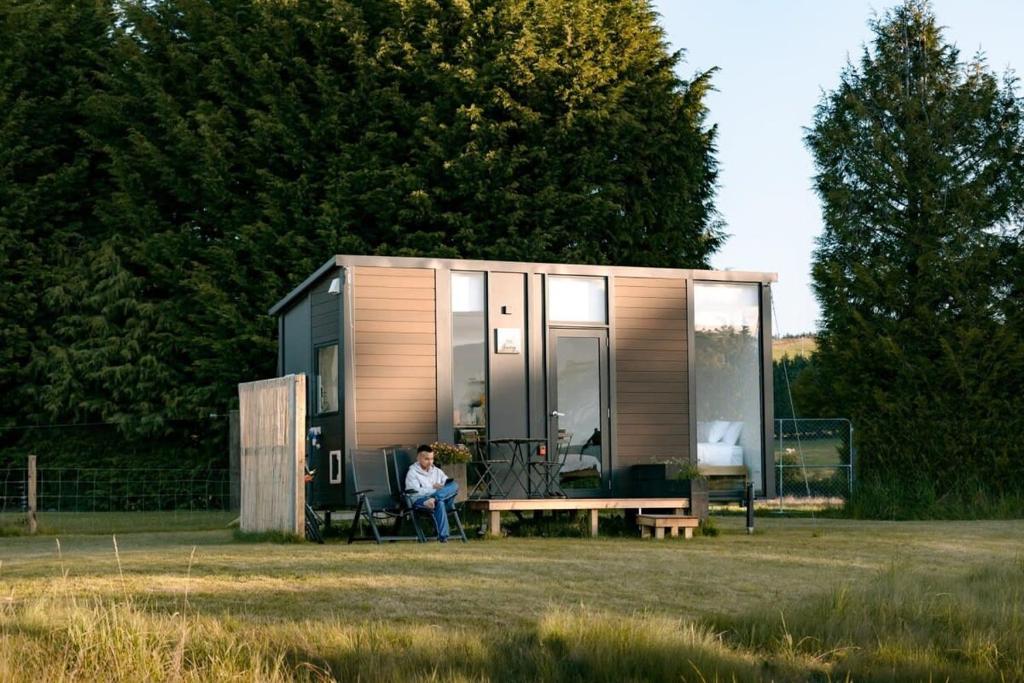 a woman sitting in a chair in front of a tiny house at Harrington's on the Terrace - Murchison in Te Anau