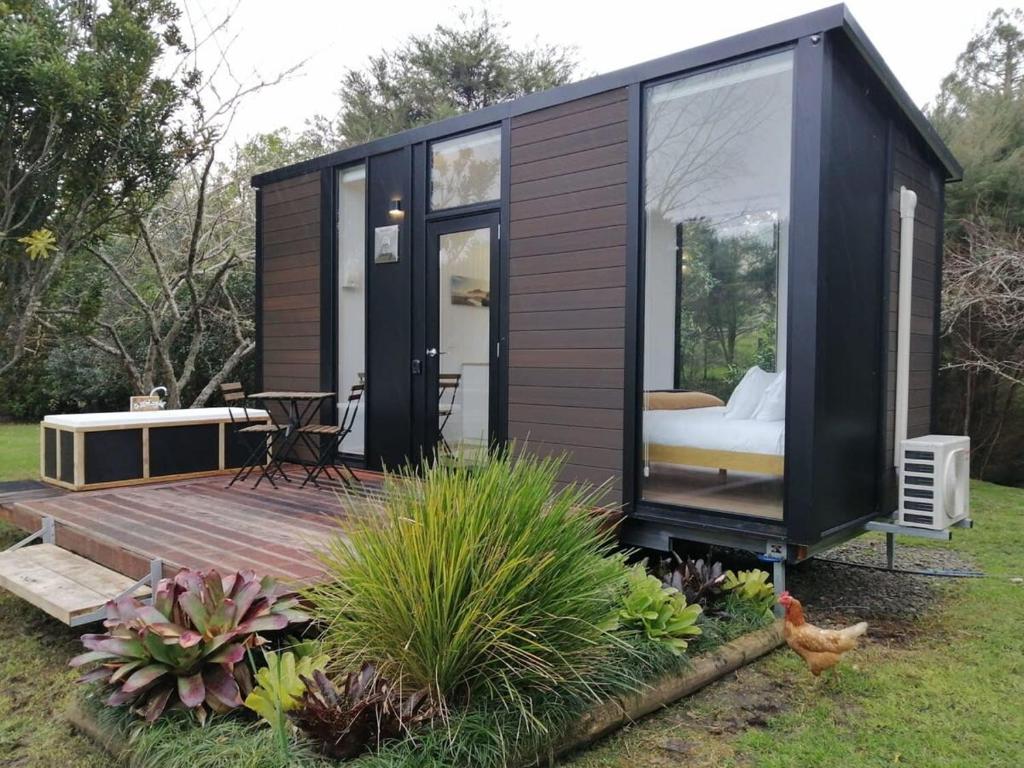 a black tiny house with a wooden deck at Creekside at Kuaotunu in Matarangi
