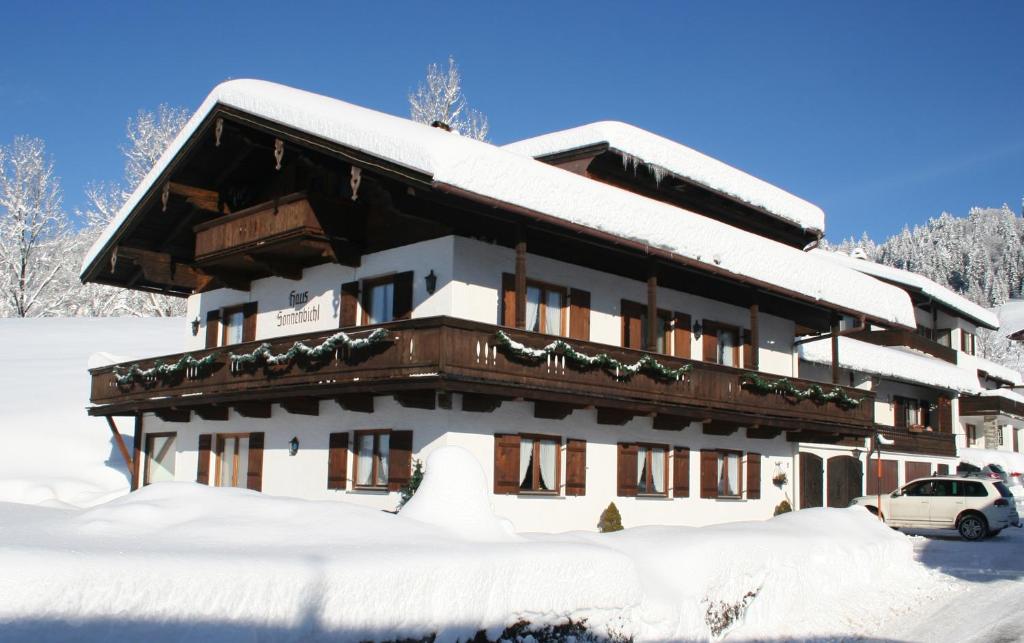 pokryty śniegiem budynek z samochodem przed nim w obiekcie Gästehaus Sonnenbichl w mieście Reit im Winkl