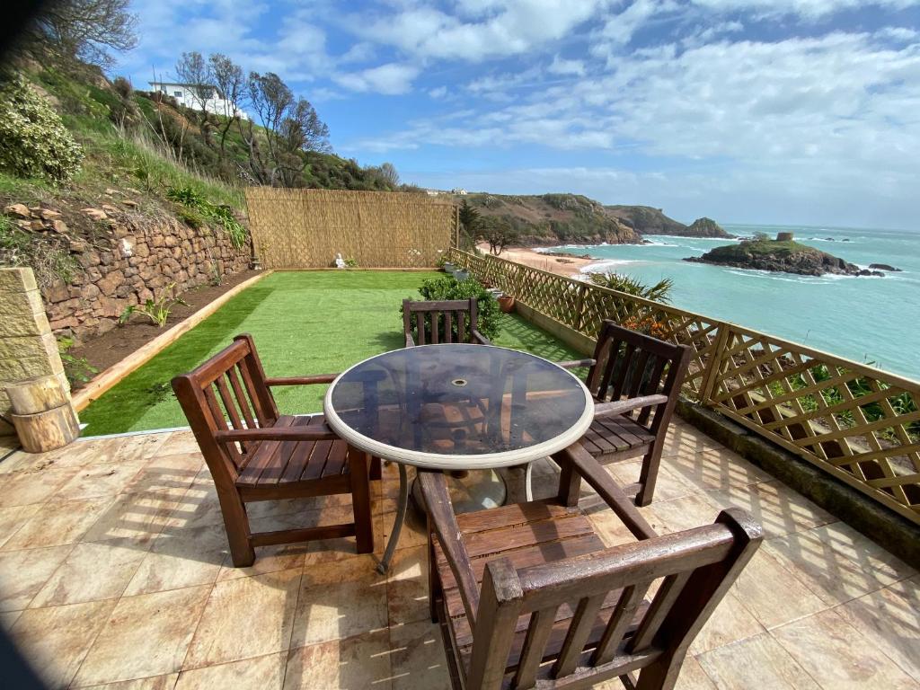un patio con mesa, sillas y el océano en Portelet Bay, en St Brelade