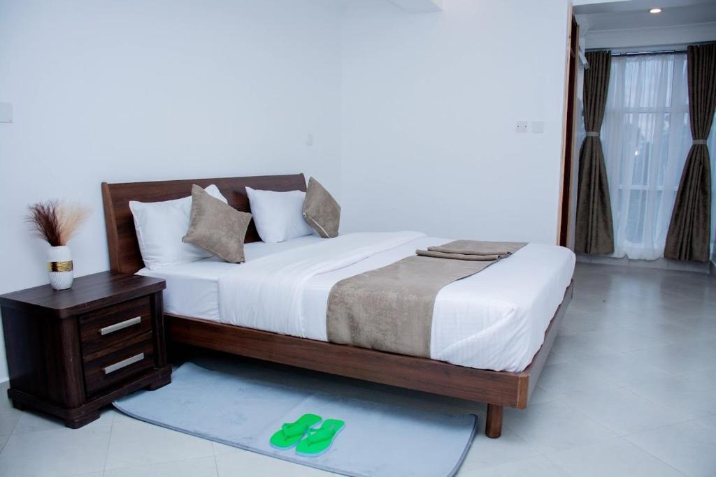 1 dormitorio con 1 cama y 1 mesa con zapatillas verdes en The Grand Rocks Hotel Limited en Eldoret