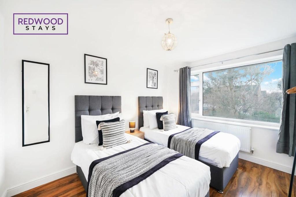 two beds in a room with a window at Cosy 3-Bedroom Serviced House with Free WiFi and Parking By Redwood Stays in Farnborough
