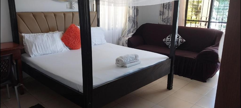 PALM SEAVIEW LUXURY HOMESTAY - SEBULENI APARTMENTS - Nyali Mombasa في مومباسا: غرفة نوم مع سرير بأربعة أعمدة وأريكة