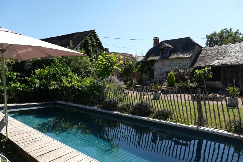 - une piscine en face d'une clôture avec un parasol dans l'établissement Les hirondelles, à Saint-Bonnet-la-Rivière