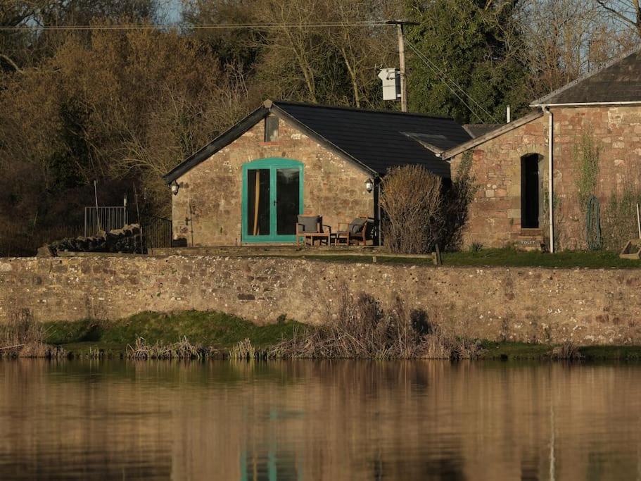 a brick house with a blue window next to a body of water at Noxon Pond Cottage in Clearwell