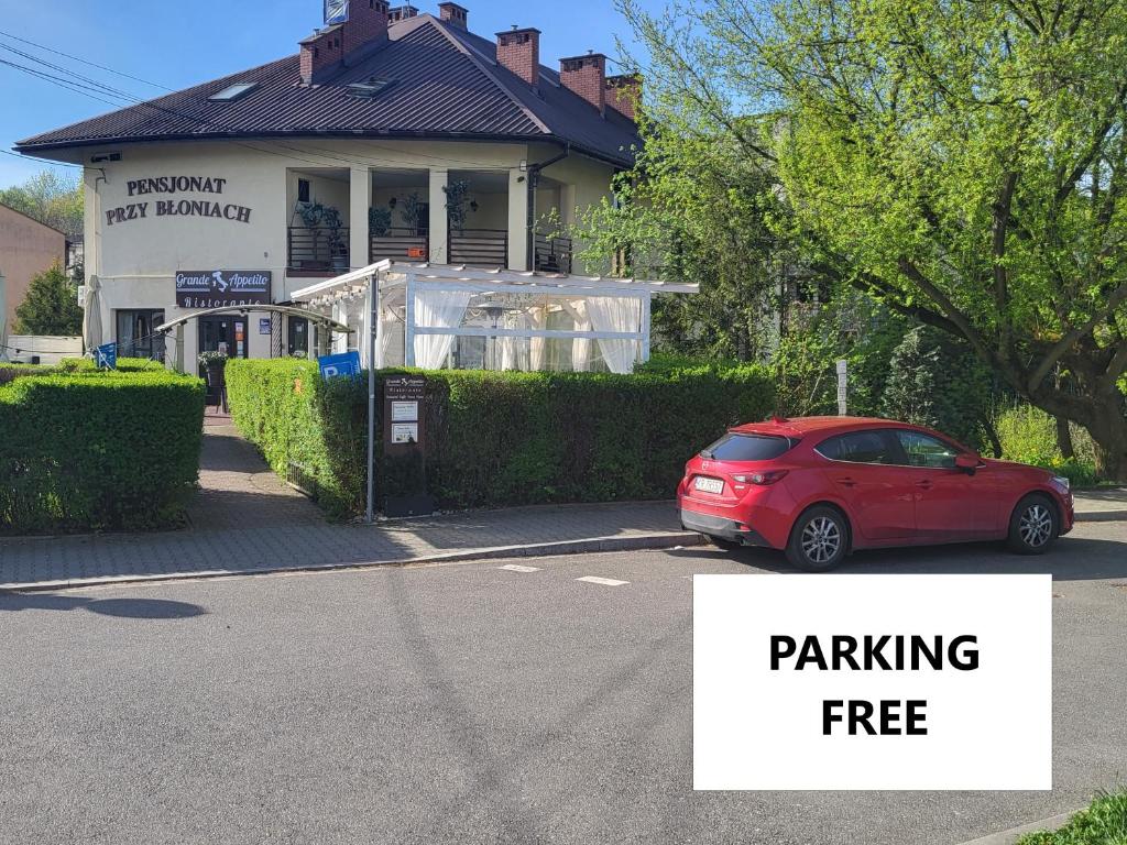 ein rotes Auto, das auf einem Parkplatz vor einem Gebäude parkt in der Unterkunft Pensjonat Przy Błoniach in Krakau