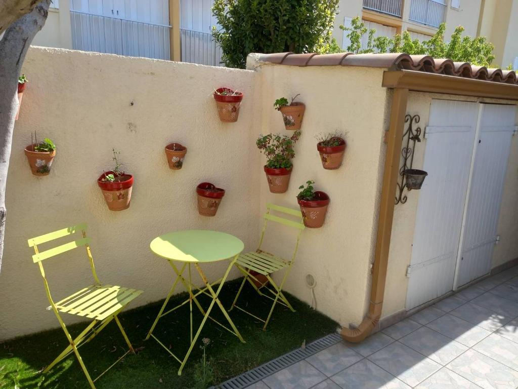 une table et des chaises à côté d'un mur avec des plantes en pot dans l'établissement HOLIDAYLAND 318 VILLA T2 MEZZANINE 4 couchages climatisé avec véranda NARBONNE PLAGE, à Narbonne-Plage