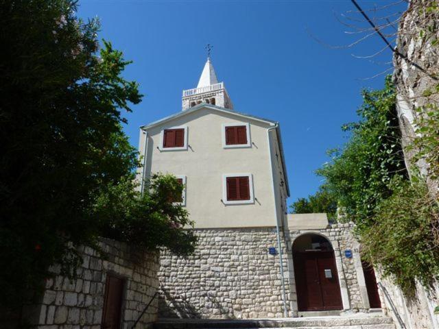 ein Gebäude mit einem Turm auf einer Steinmauer in der Unterkunft Apartment Pulić in Rab