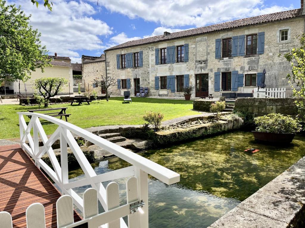 un bâtiment avec un pont et un étang en face dans l'établissement Petit Moulin De Veillard, à Bourg-Charente