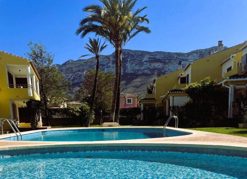 uma piscina com uma palmeira e montanhas ao fundo em El casa KáMa em Denia