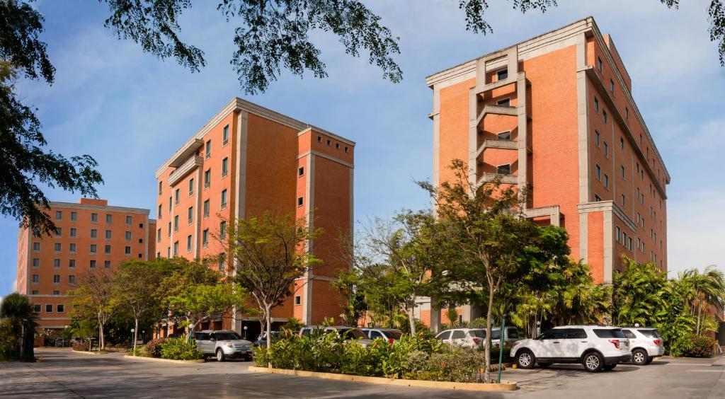 zwei hohe Gebäude mit Autos auf einem Parkplatz in der Unterkunft Hotel GH Guaparo INN in Naguanagua