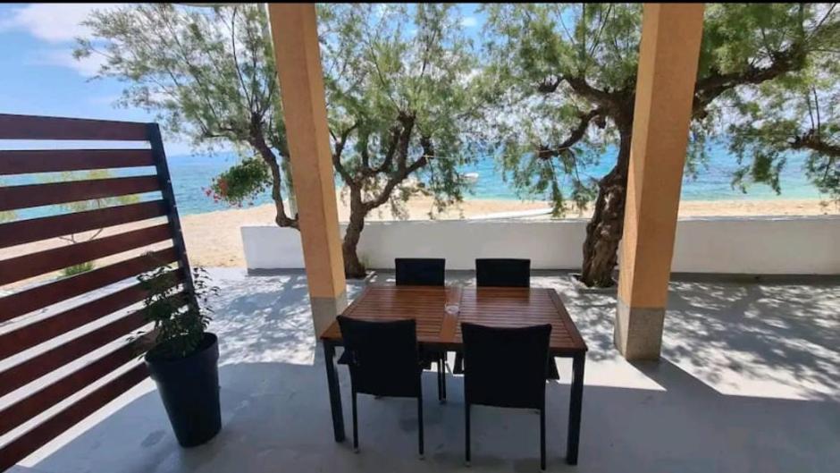 een houten tafel en stoelen op een patio met uitzicht op het strand bij Beach apartment Perisic Podstrana in Podstrana