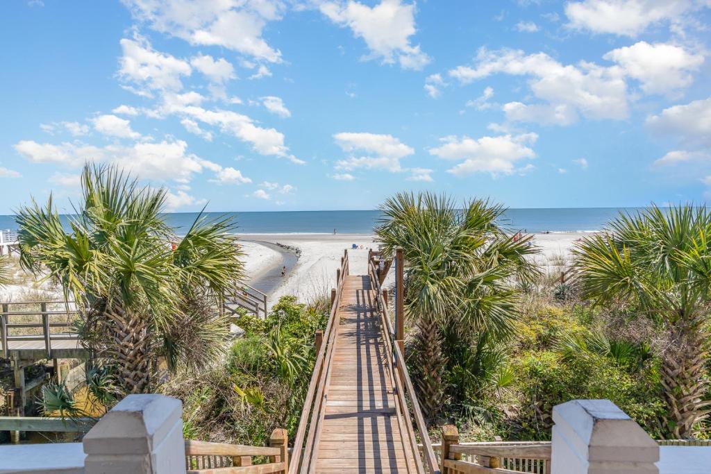 a wooden walkway to the beach with palm trees at 311B - True Beachfront w/ Private Walkway and Pool in Myrtle Beach