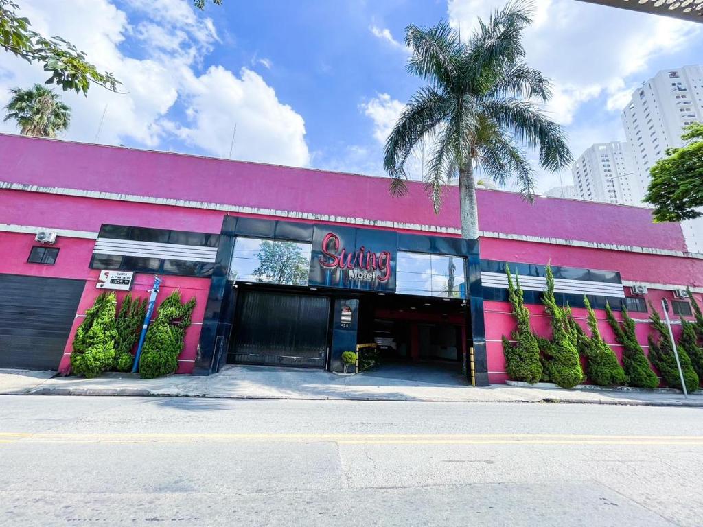 a pink building with a palm tree in front of it at Swing Motel 1 in Sao Paulo