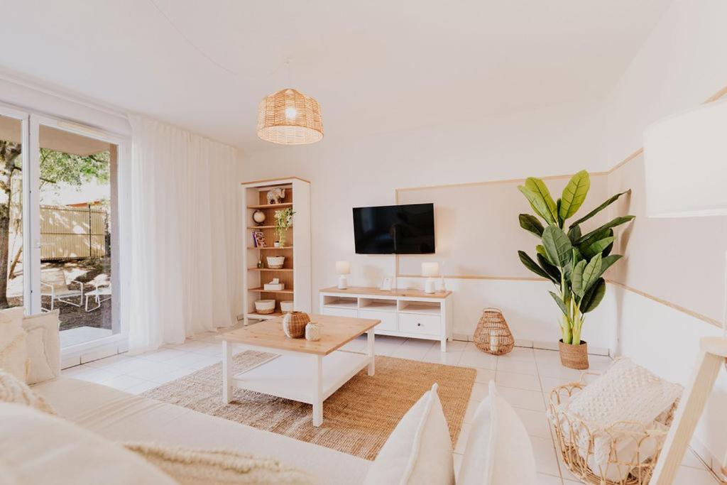 ein weißes Wohnzimmer mit einem TV und einem Tisch in der Unterkunft Le Cocon de Lespinasse - Parking - Checkin Autonome in Lespinasse