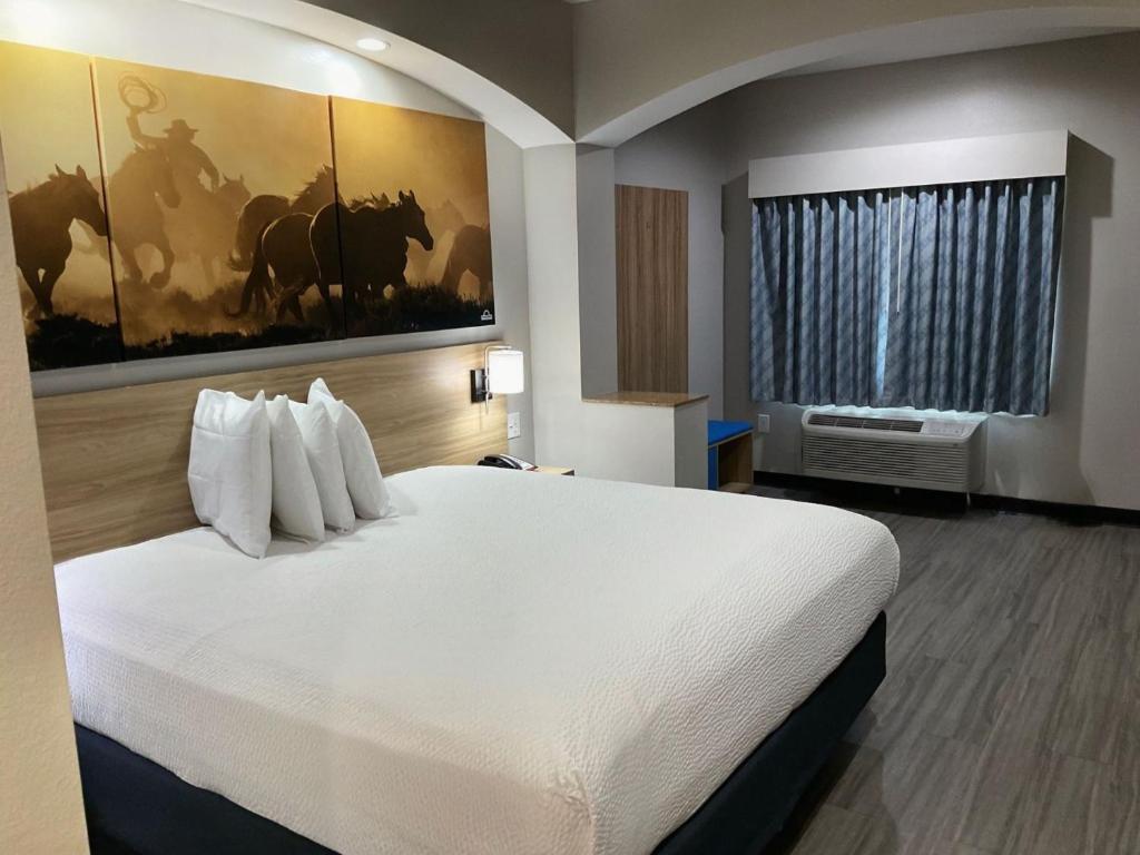 a bedroom with a large white bed with a painting on the wall at Days Inn by Wyndham Humble/Houston Intercontinental Airport in Humble