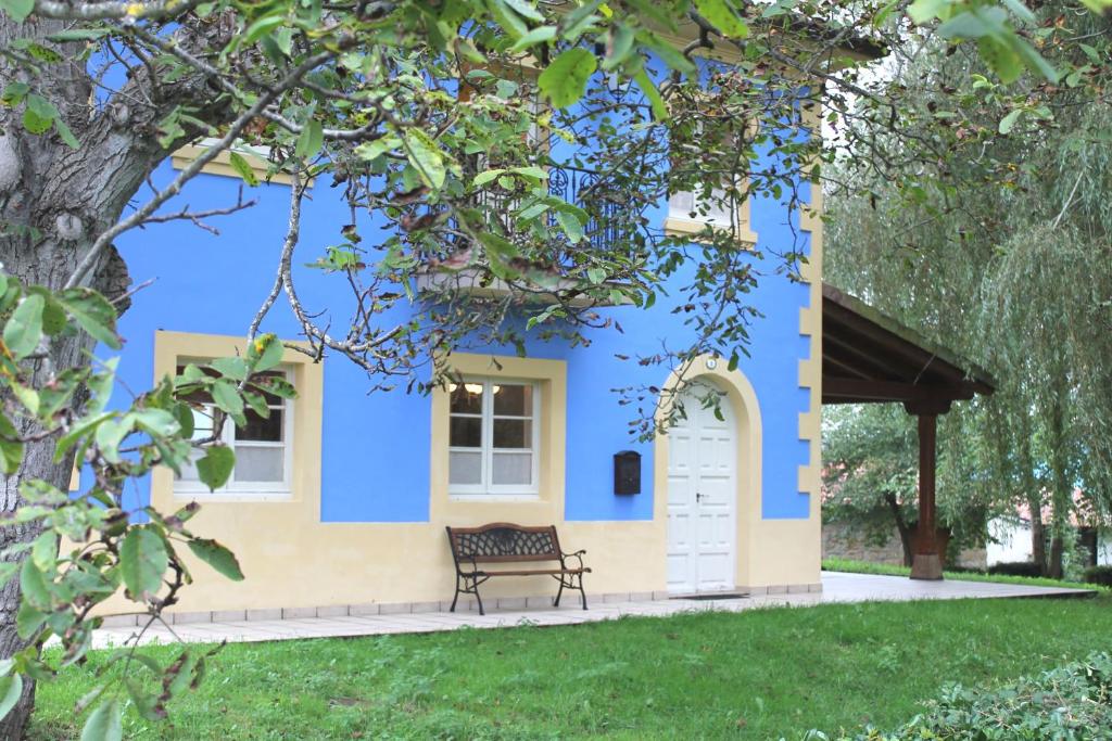 una casa azul y amarilla con un banco en el patio en Casa de Aldea Monga 9 en Nava, Asturias, en Nava