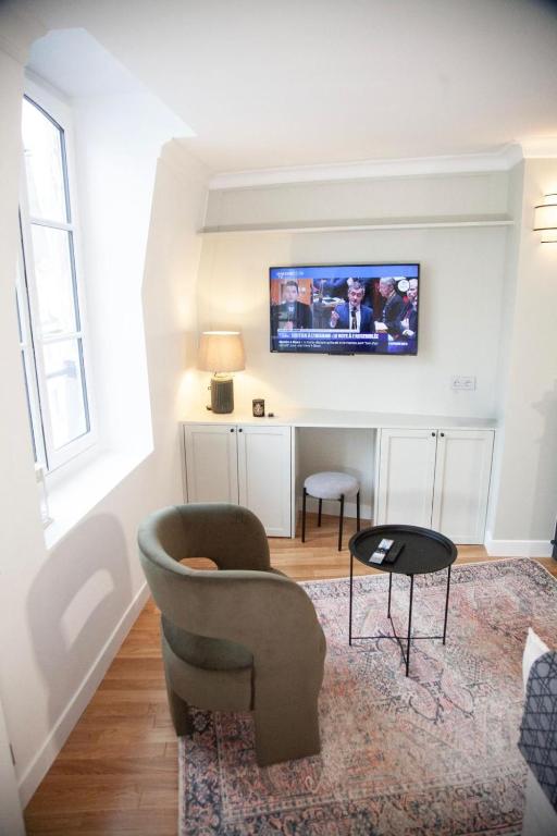 Elle comprend un salon avec une chaise et une télévision murale. dans l'établissement Au Cœur de Paris, à Paris