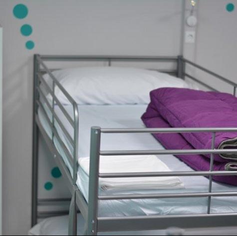 a metal bunk bed with white sheets and purple pillows at Albergue Augas Quentes in Ourense