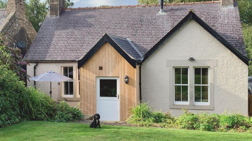 a black dog sitting in front of a house at Pentland Cottage in Norham