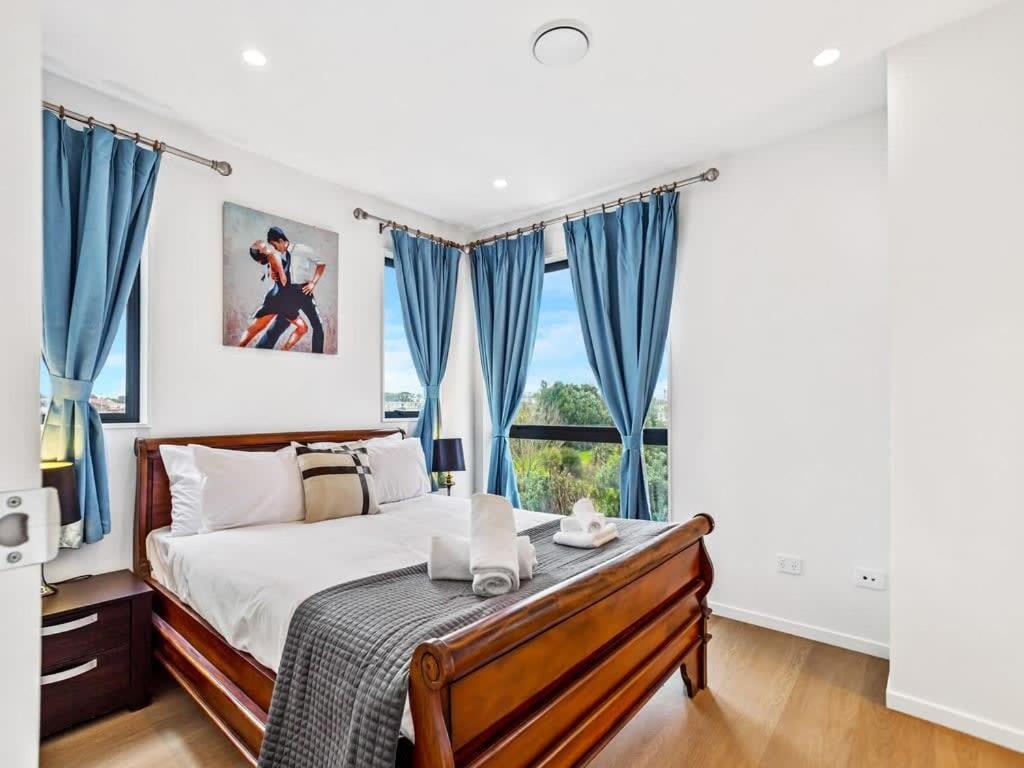 a bedroom with a bed with blue curtains and a window at Gorgeous Three Bedroom Home with Free Parking in Auckland