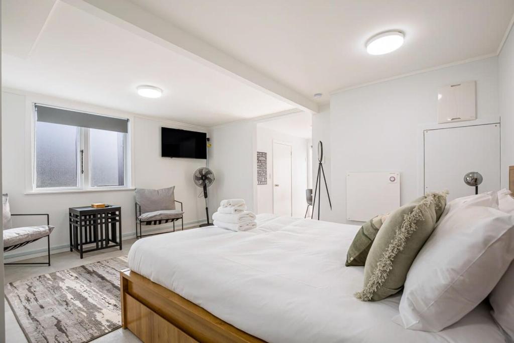 a white bedroom with a large bed and a chair at Stunning studio in Grey Lynn in Auckland