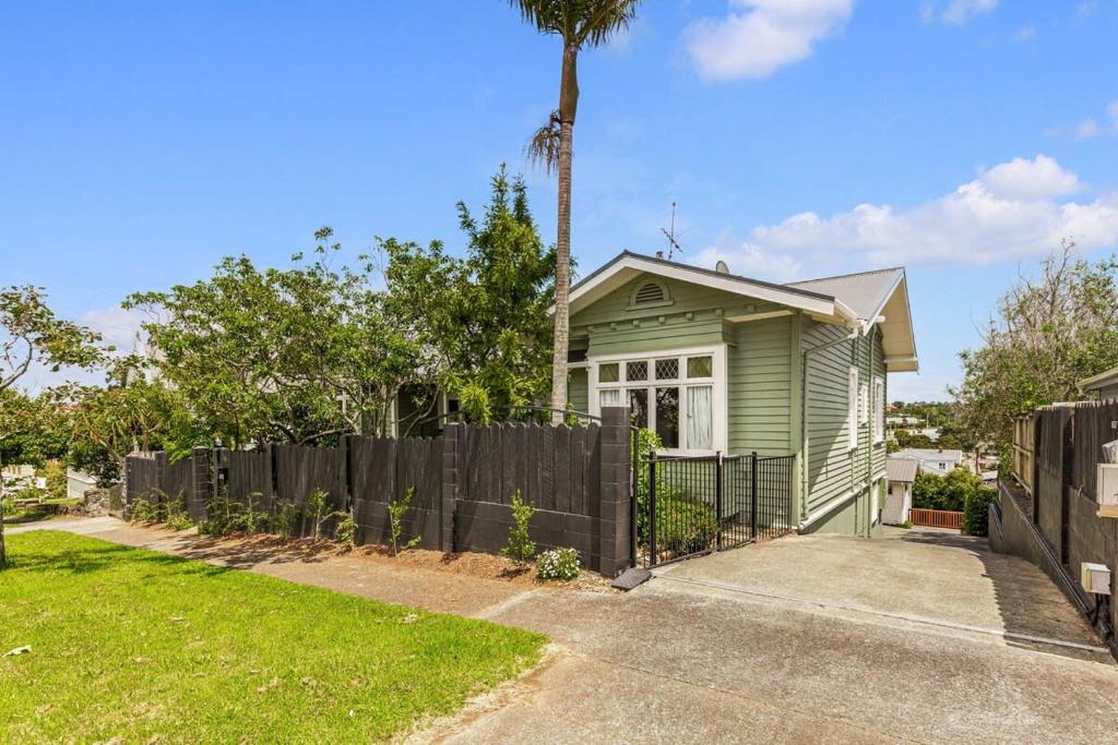 a green house with a fence and a palm tree at Character-Filled Home w Parking in Auckland
