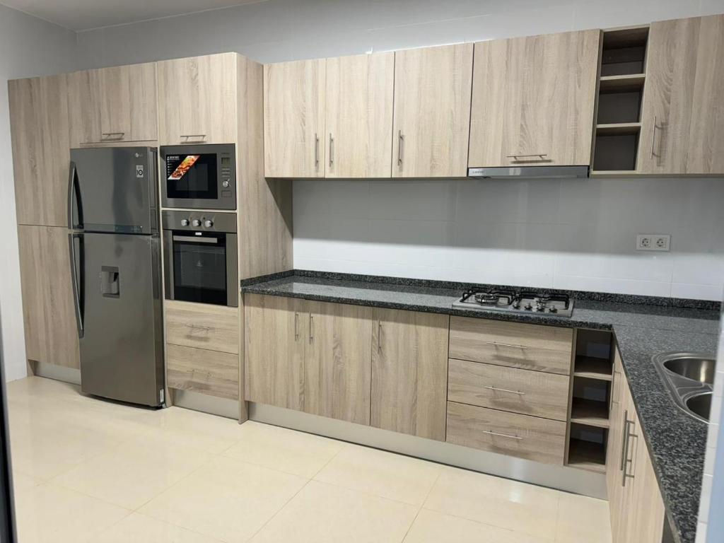 a kitchen with wooden cabinets and a stainless steel refrigerator at BemVinda Sweet Home - Cama Mesa e Fogão in Praia