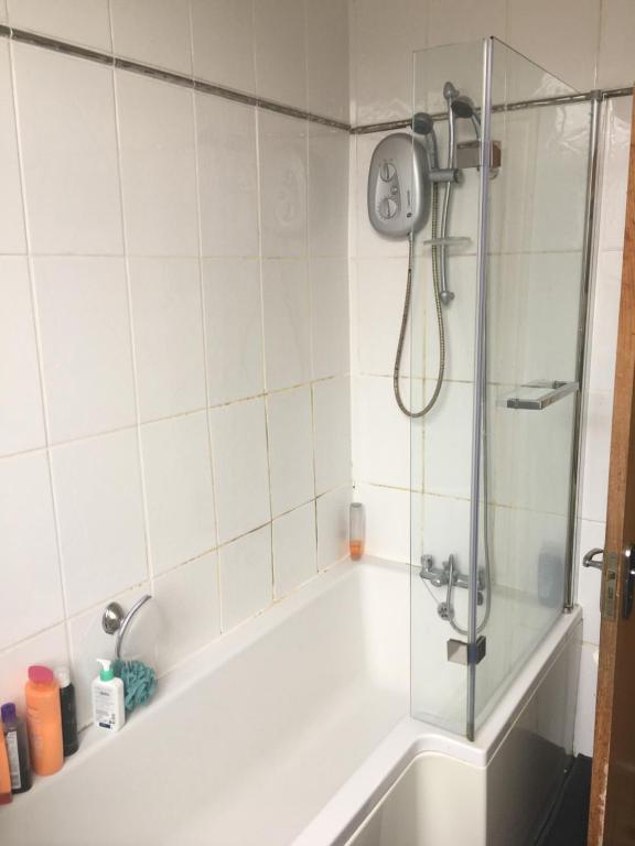 a bath tub with a shower with a glass door at Double room near City Centre in Manchester