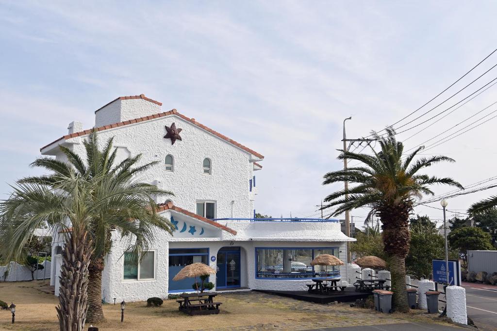 a white building with palm trees in front of it at Sweet Stay Pension in Seogwipo