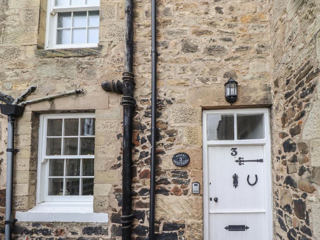 ein Backsteingebäude mit einer weißen Tür und zwei Fenstern in der Unterkunft Avocet Cottage in Bamburgh