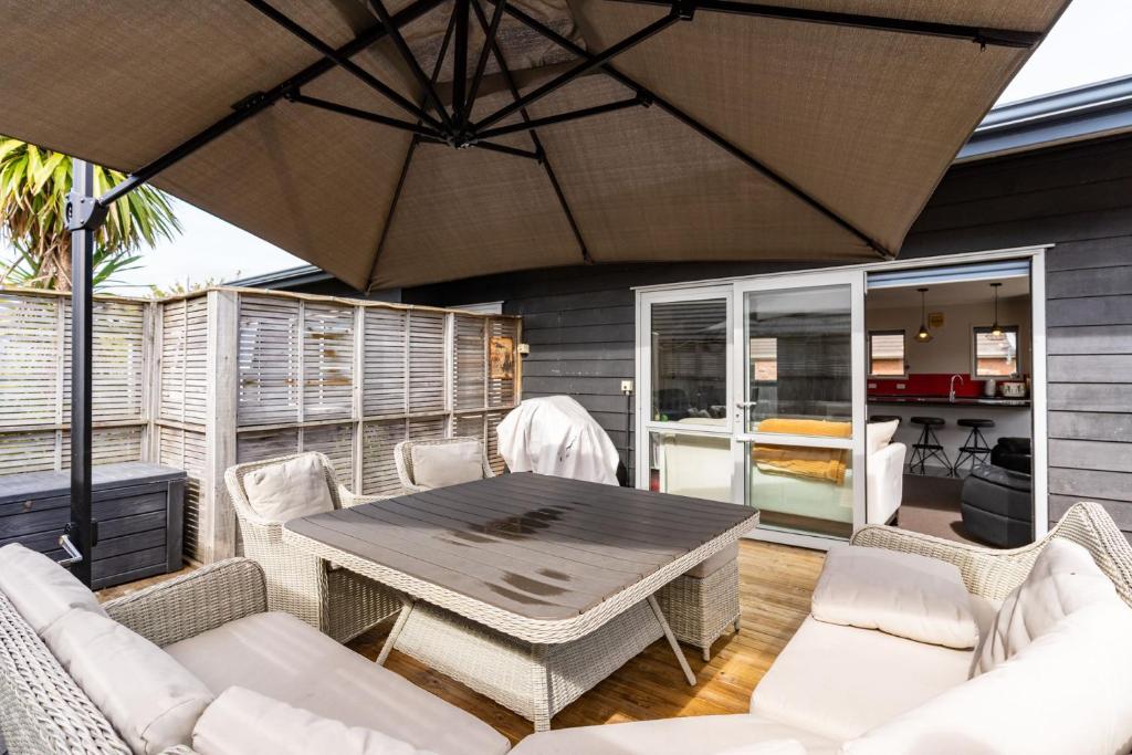 een patio met een tafel en stoelen en een parasol bij Kaya-wai - Mangawhai Holiday Home in Mangawhai