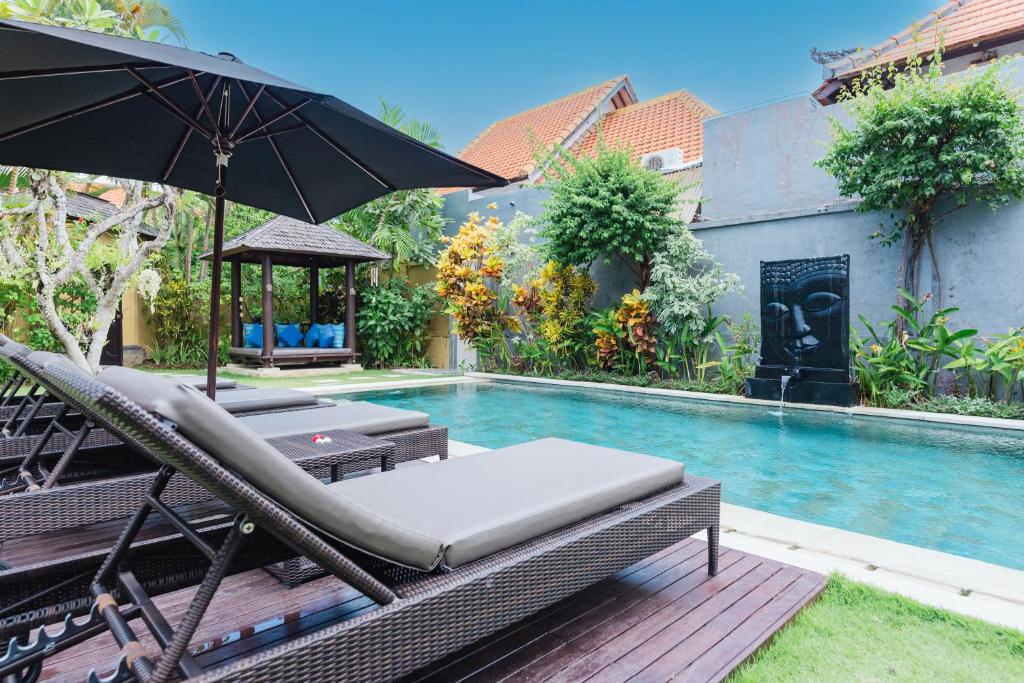 a swimming pool with chairs and an umbrella next to a swimming pool at The Zen Villas in Sanur